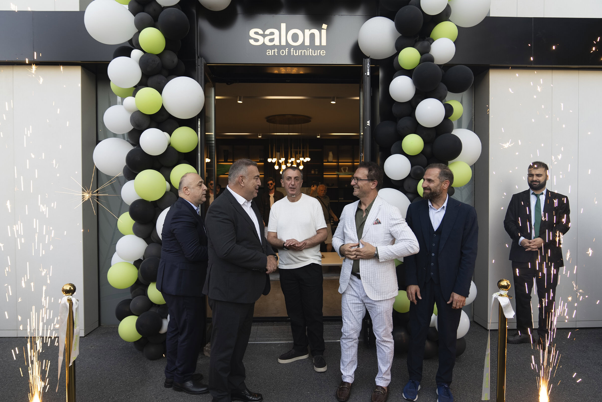 Elegant indoor event celebrating the opening of Saloni Furniture showroom with stylish apparel, balloon arch decorations in black, white, and green, and sparklers to mark the occasion.