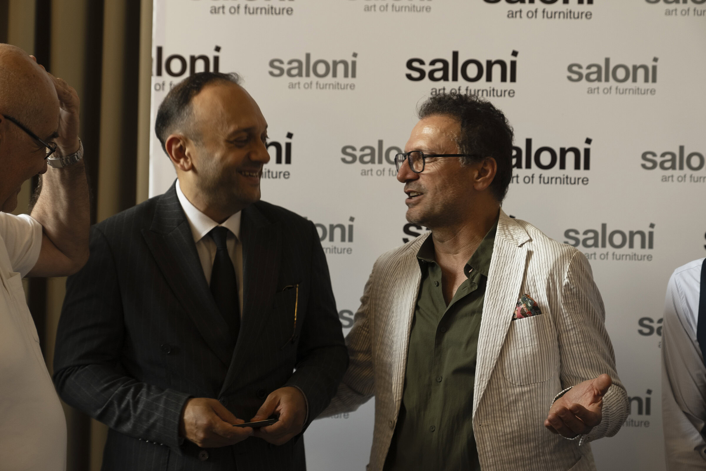 Modern businessman discussing at Saloni Furniture event with a branded backdrop.